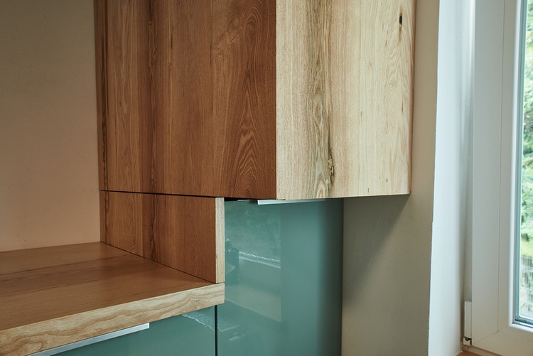 Detaliu cu imbinarea dintre blatul din lemn si un corp inalt din lemn masiv de frasin cu aspect natural. Corpurile inferioare sunt de culoare verde oliv.