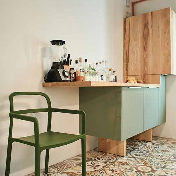 interior de bucatarie cu scaun verde, pardoseala cu gresie cu motive florale, corpuri de mobila verde oliv cu picioare masive, blat și uși din lemn de frasin cu finisaj natural