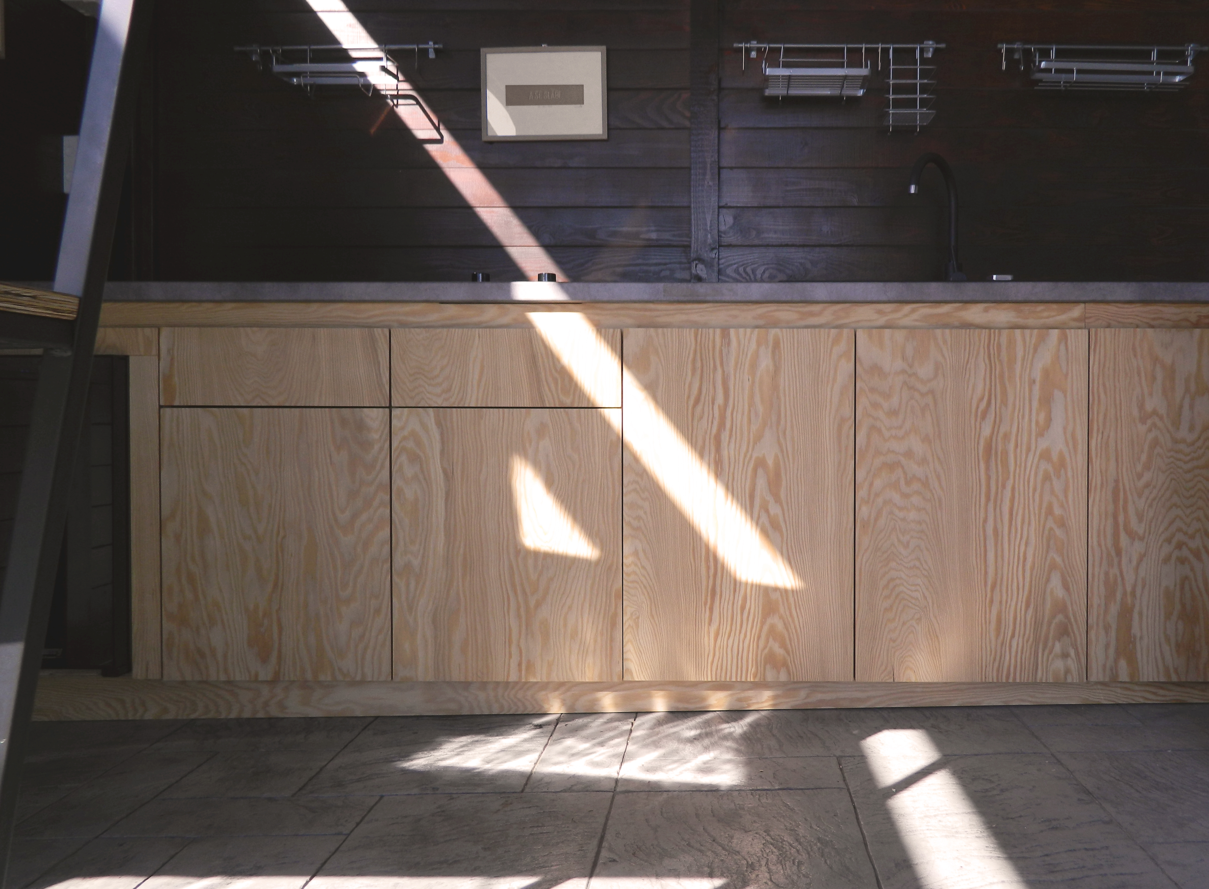 vedere frontala cu corp de bucatarie din placaj de larice cu fibre naturale de lemn vizibile, cu fundal de lambriu de culoare inchisa